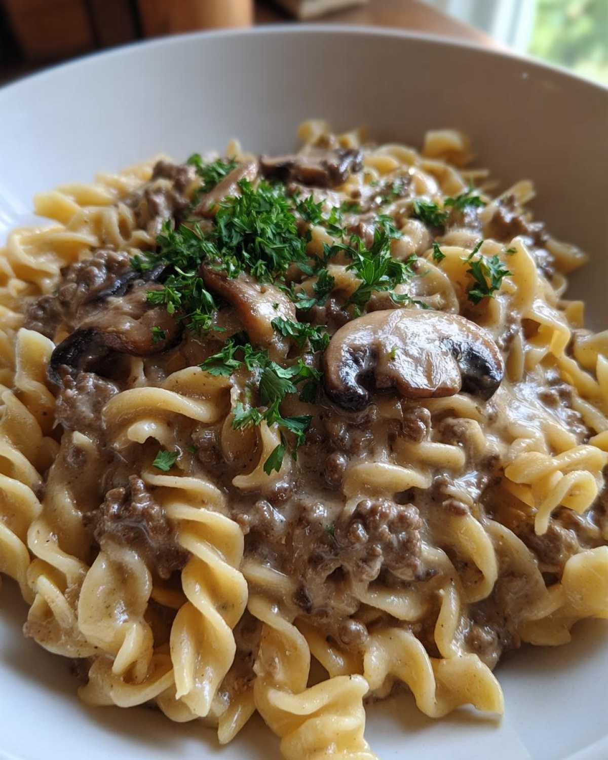 Close-up of One Pan Ground Beef Stroganoff mixed with rotini pasta, topped with sliced mushrooms and fresh parsley.