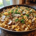 A close-up of One Pan Ground Beef Stroganoff with egg noodles, ground beef, mushrooms, and parsley in a black skillet.