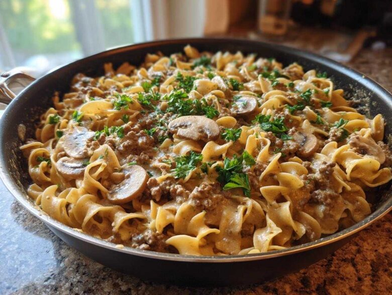 A close-up of One Pan Ground Beef Stroganoff with egg noodles, ground beef, mushrooms, and parsley in a black skillet.