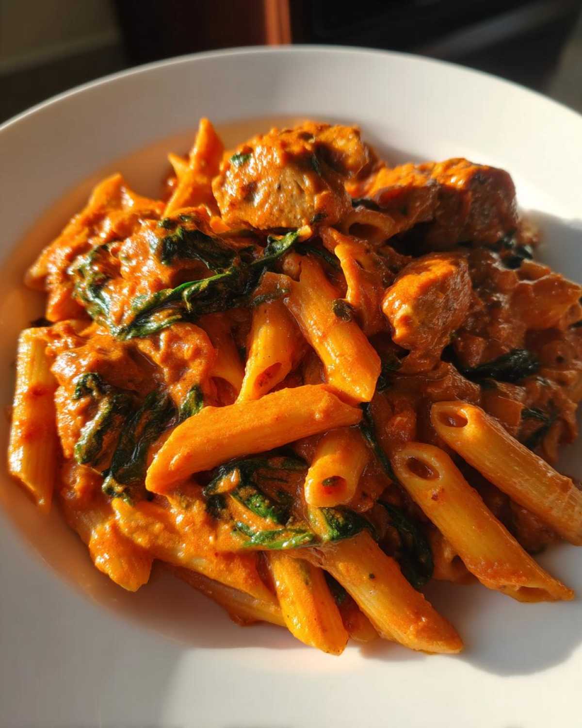 Close-up of One Pot Creamy Tomato Pasta with Chicken mixed with wilted spinach in a white bowl.