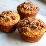 Three golden brown Pecan Pie Brown Sugar Muffins topped with pecans and coarse sugar crystals.