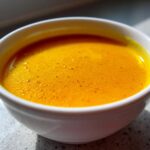 Close-up of a white bowl filled with vibrant orange Simple Roasted Butternut Squash Soup.