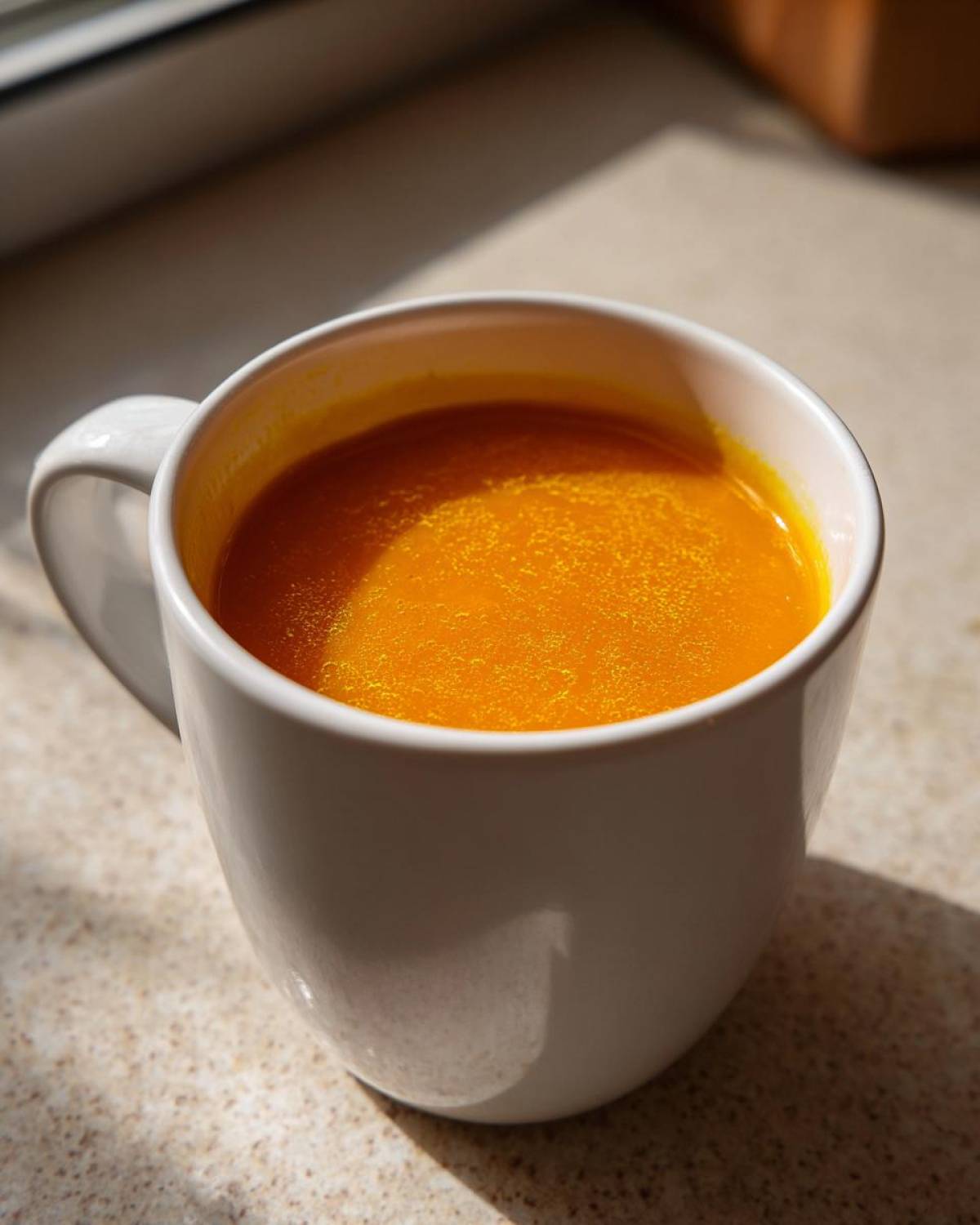 Close-up of bright orange Simple Roasted Butternut Squash Soup served in a white mug.
