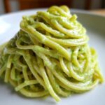 A mound of spaghetti coated in a vibrant, creamy Italian Zucchini Sauce served on a white plate.