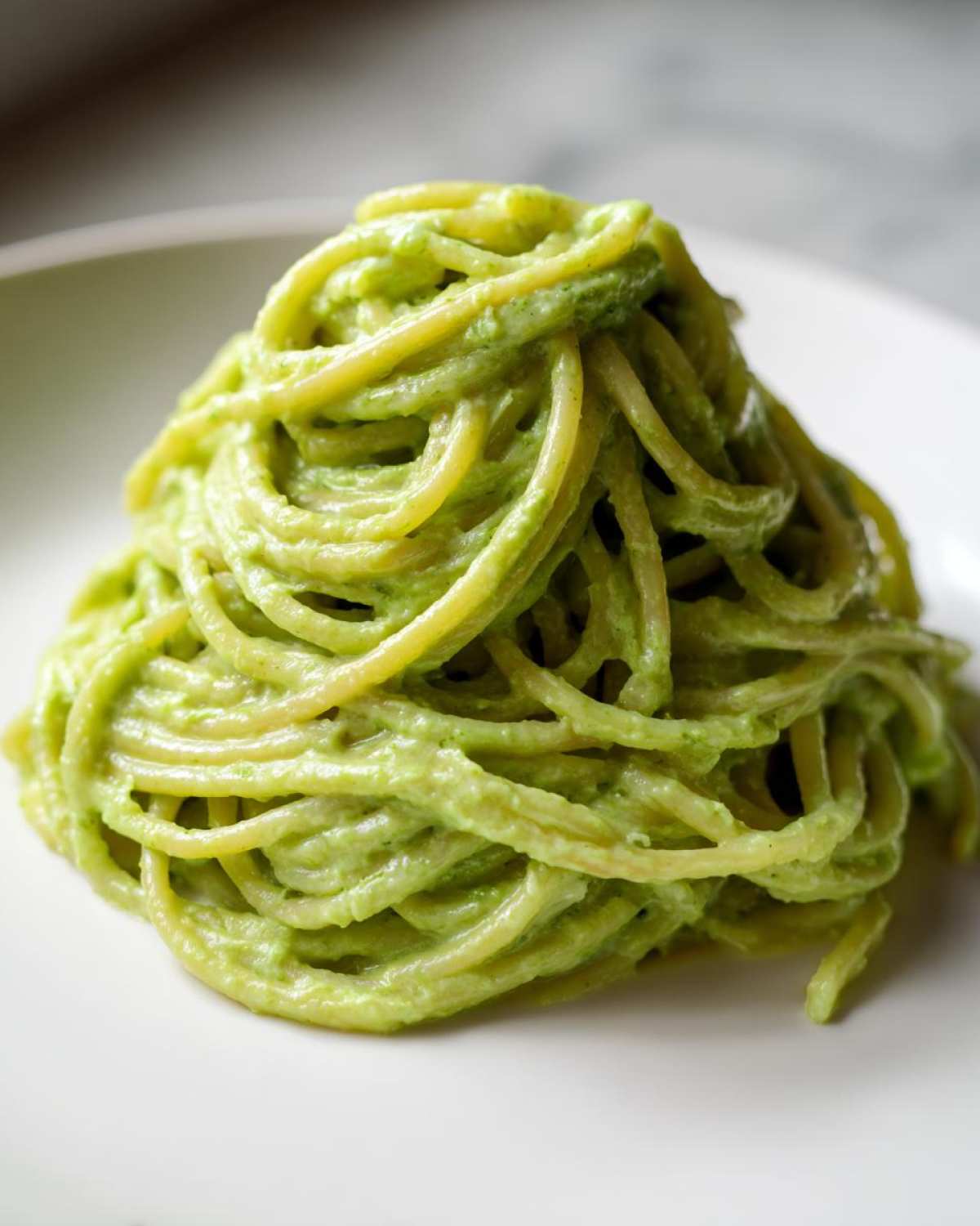 A mound of spaghetti coated in a vibrant, creamy Italian Zucchini Sauce served on a white plate.