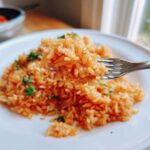 A fork lifting a bite of perfectly cooked, orange-colored Spanish rice garnished with parsley.