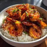 Close-up of a white bowl filled with white rice topped generously with glossy Spicy Honey Garlic Shrimp and garnished with green onions.