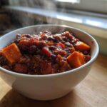 A close-up of a steaming white bowl filled with hearty Vegan Chili Recipe, featuring chunks of sweet potato and kidney beans.