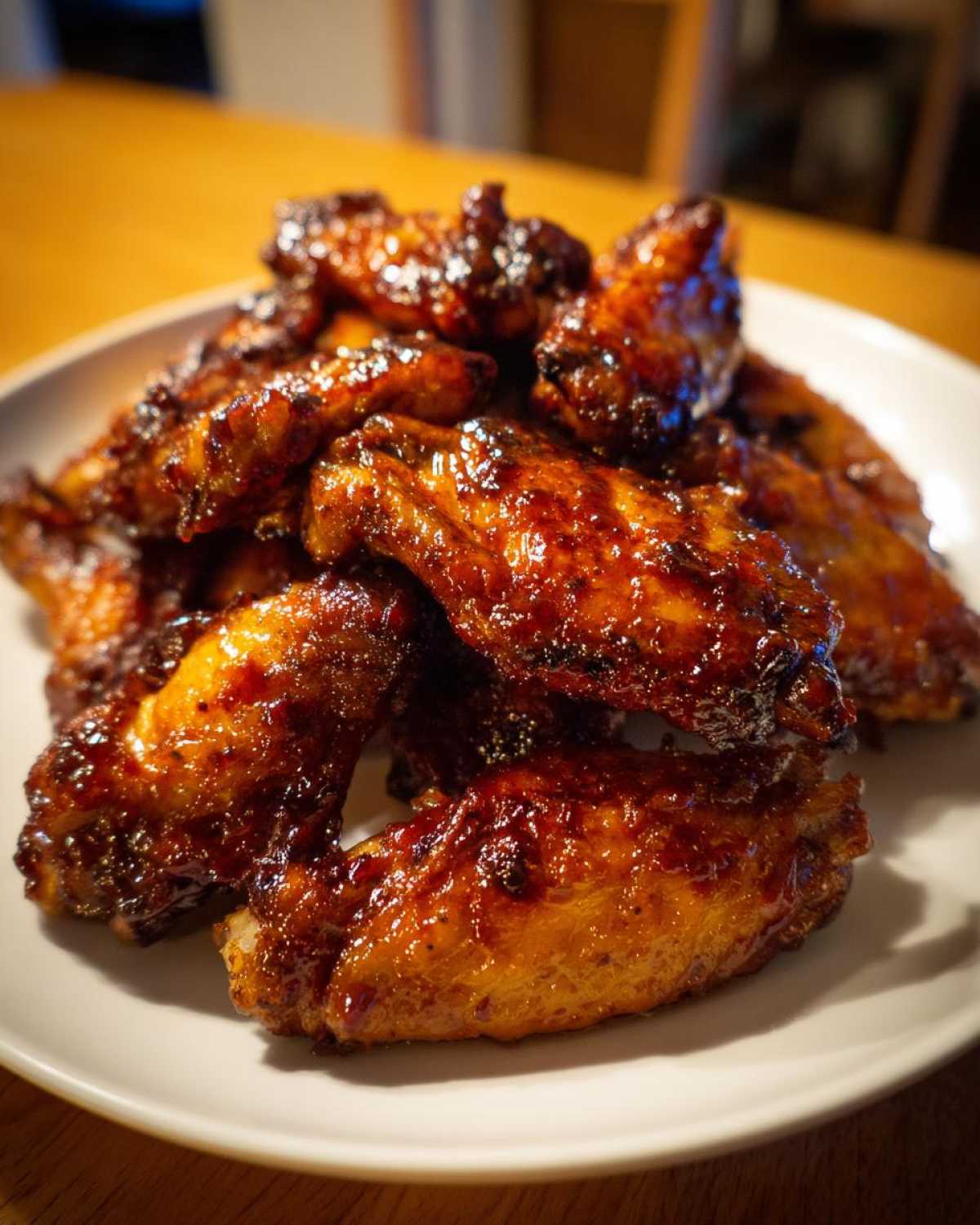 A pile of perfectly cooked Sticky BBQ Chicken Wings Crispy Oven Style glistening with dark, caramelized sauce on a white plate.