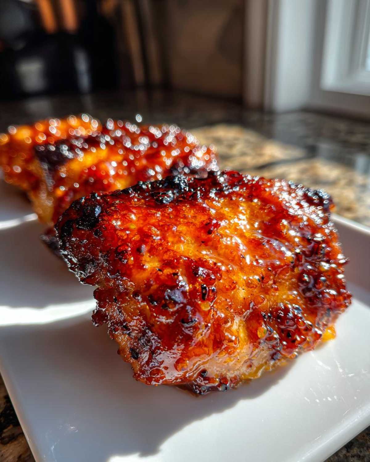 Two pieces of beautifully glazed Sticky Orange Chicken Thighs showing a caramelized, shiny orange coating.