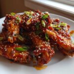 A plate piled high with Sticky Orange Chicken Wings with Honey Glaze, coated in a shiny sauce and sprinkled with sesame seeds and green onions.