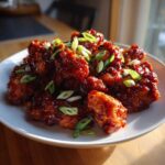 Close-up of crispy chicken pieces coated in a glossy, dark red sauce, garnished with sliced green onions, part of the Sticky Sweet Chili Chicken Easy Recipe.