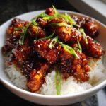 Close-up of Sticky Sweet Chili Chicken Skillet pieces coated in dark glaze, served over white rice and garnished with green onions and sesame seeds.