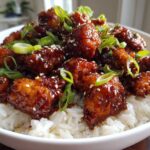 Close-up of Sticky Sweet Chili Chicken Skillet pieces coated in glossy sauce, served over white rice and garnished with green onions and sesame seeds.