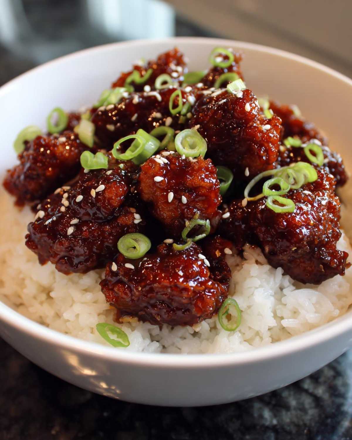 Close-up of Sticky Sweet Chili Chicken Skillet pieces coated in dark glaze served over white rice and garnished with green onions and sesame seeds.