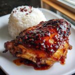 A close-up of Sticky Sweet Chili Chicken Thighs glazed with a thick, spicy sauce, served next to a mound of white rice.