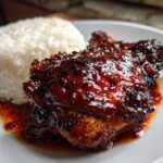 Close-up of a glazed Sticky Sweet Chili Chicken Thighs served next to a mound of fluffy white rice on a white plate.