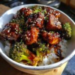 A close-up of a Sticky Teriyaki Chicken Bowl featuring glazed chicken pieces, roasted broccoli, and white rice, topped with sesame seeds.
