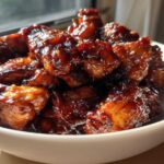 Close-up of glossy, dark brown Sticky Teriyaki Chicken Easy Weeknight Meal pieces piled high in a white bowl.
