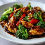 Close-up of tender chicken pieces coated in thick sauce with bright green broccoli and red peppers in a Sticky Teriyaki Chicken Stir Fry Quick Meal.