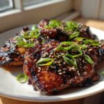 Three glistening Sticky Teriyaki Chicken Thighs topped with sesame seeds and sliced green onions.