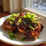 Two glazed chicken thighs covered in a sticky sauce, sesame seeds, and fresh green onions, representing Sticky Teriyaki Chicken Thighs.