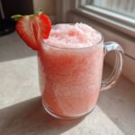 A frosty glass mug filled with Irresistible Strawberry Pina Colada Punch, garnished with a fresh strawberry slice.