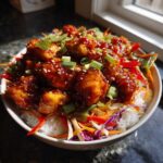 A close-up of a Sweet Chili Chicken Bowl with crunchy veggies, featuring glazed chicken pieces over rice, garnished with sesame seeds and scallions.
