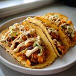 Three delicious Sweet Potato and Black Bean Tacos topped with creamy sauce and shredded lettuce.