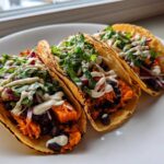 Three delicious Sweet Potato and Black Bean Tacos filled with orange sweet potato, black beans, red onion, greens, and drizzled with white sauce.
