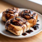 Three freshly baked Coffee Rolls drizzled generously with a rich, dark coffee glaze, served on a light plate.