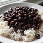 Close-up of a white bowl filled with fluffy white rice topped generously with rich, dark Black Beans and Rice.