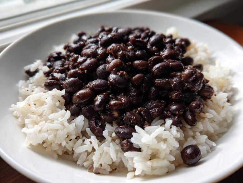 Close-up of a white bowl filled with fluffy white rice topped generously with rich, dark Black Beans and Rice.