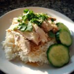 A plate featuring moist, sliced poached chicken served over fragrant rice, garnished with fresh cilantro, making up a perfect Chicken Rice dish.