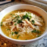 Close-up of a white bowl filled with amazing Chicken Rice Soup, topped with shredded chicken, rice, and fresh parsley.