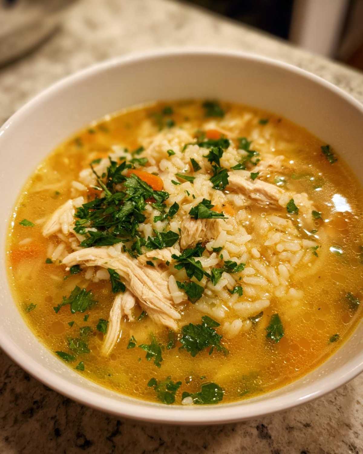 Close-up of a white bowl filled with amazing Chicken Rice Soup, featuring shredded chicken, rice, carrots, and fresh parsley.