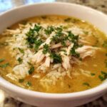 Close-up of a white bowl filled with amazing Chicken Rice Soup, featuring shredded chicken, white rice, and fresh parsley garnish.