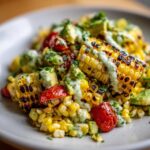Close-up of a vibrant Corn Salad featuring grilled corn cob pieces, avocado chunks, and cherry tomatoes drizzled with a creamy green sauce.
