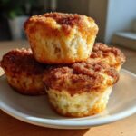 Three Apple Cinnamon Greek Yogurt Muffins stacked on a white plate, featuring a crunchy cinnamon-sugar topping.