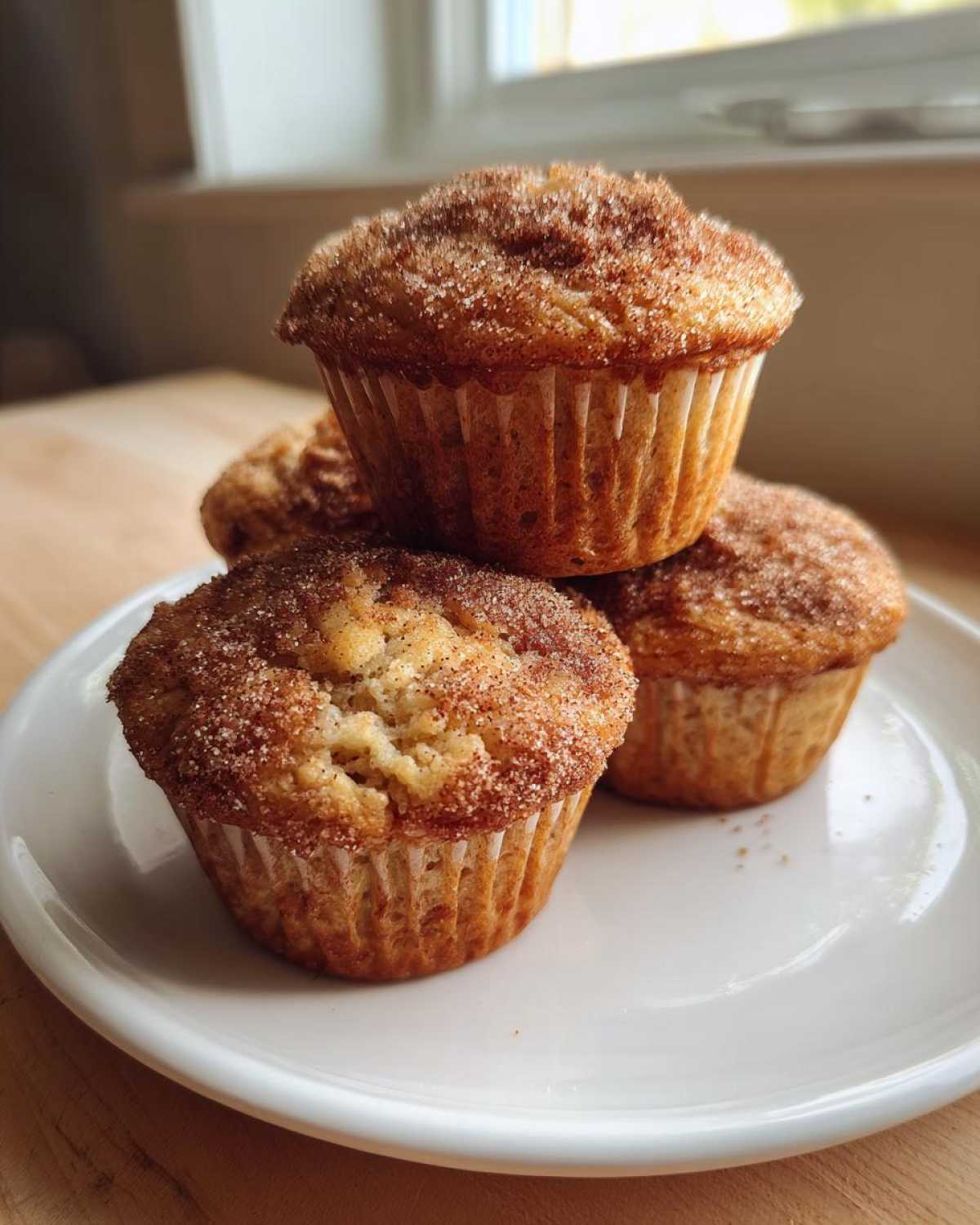 A small stack of four Apple Cinnamon Greek Yogurt Muffins topped with a cinnamon sugar crust on a white plate.