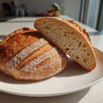 A whole loaf of Bakery Style French Bread with a crackly crust, next to a slice showing an open, airy crumb structure.