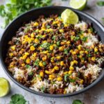 A close-up overhead shot of flavorful Black Bean & Corn Rice topped with cilantro and lime wedges.