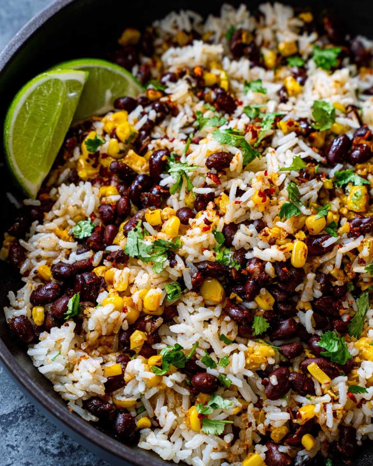 A close-up bowl of flavorful Black Bean & Corn Rice, garnished with fresh cilantro and a lime wedge.
