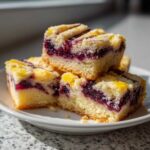 Three stacked squares of moist Blackberry Shortbread Wedges featuring a thick layer of dark purple blackberry filling and a crumbly topping.