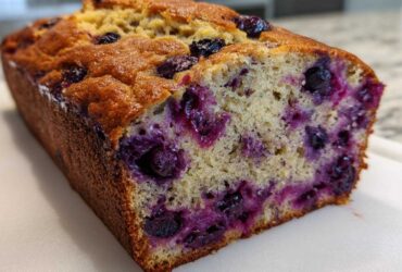 A close-up of a freshly baked Blueberry Banana Bread loaf showing a moist, tender crumb loaded with purple blueberries.