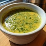 Close-up of a white bowl filled with vibrant, creamy Broccoli and Cheddar Soup, showing flecks of green broccoli.