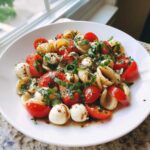 A vibrant bowl of Caprese Pasta Salad featuring shell pasta, cherry tomatoes, mozzarella balls, and fresh basil drizzled with balsamic glaze.