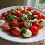 Close-up of fresh cherry tomatoes, mozzarella balls, and basil in a balsamic glaze, perfect for Caprese Pasta Salad.