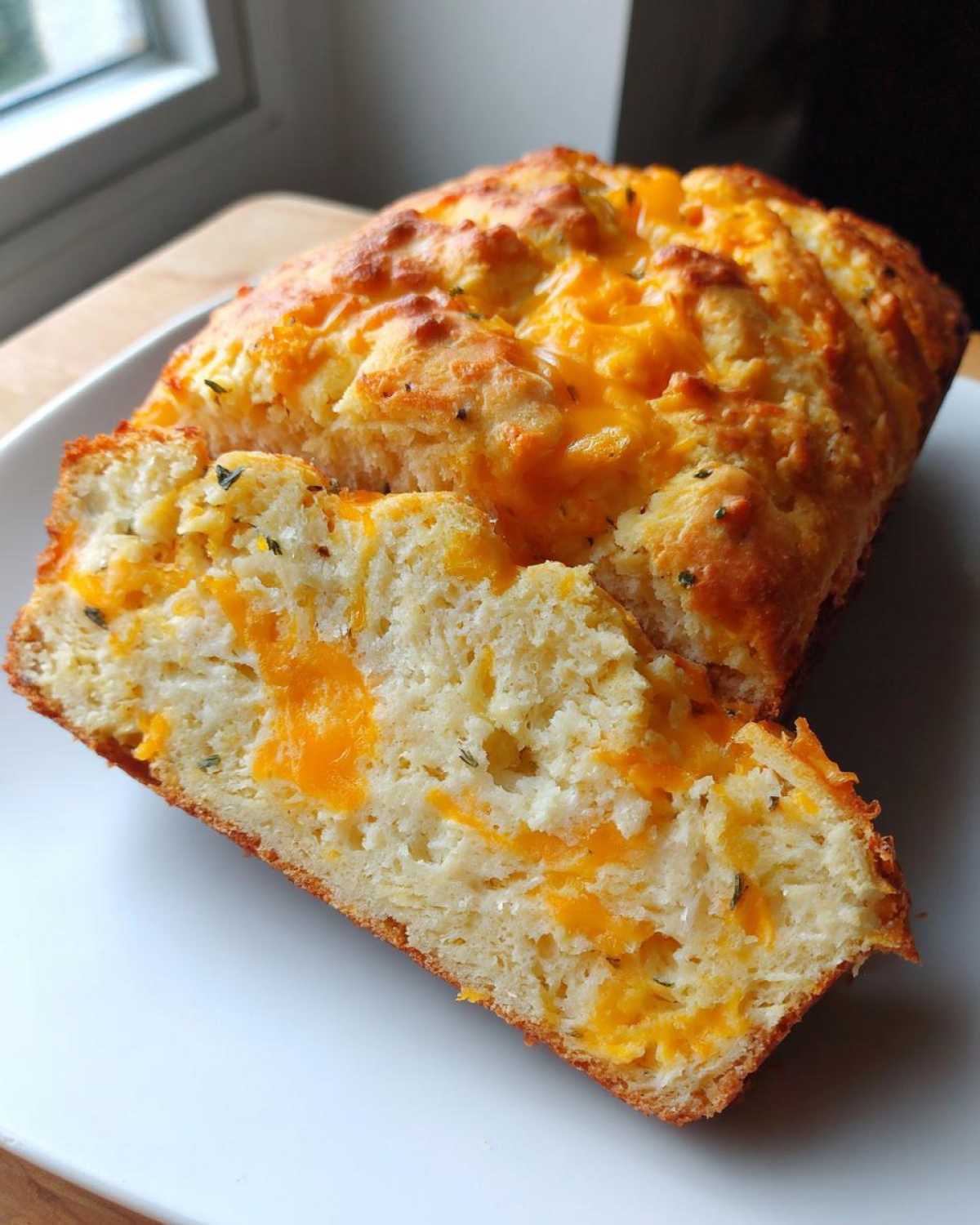 A slice cut from a golden brown Cheese Bread Quick Bread 30 Minutes loaf, showing melted cheddar cheese inside.