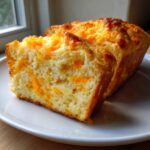 A thick slice cut from a loaf of amazing Cheese Bread Quick Bread 30 Minutes, showing melted orange cheddar cheese throughout the crumb.